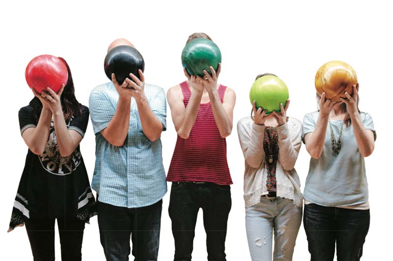 Five people standing in a line holding bowling balls covering their faces