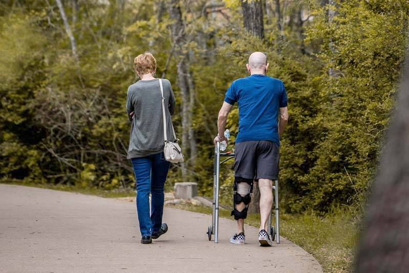 Couple walking along a path in a forest with the man using a walker